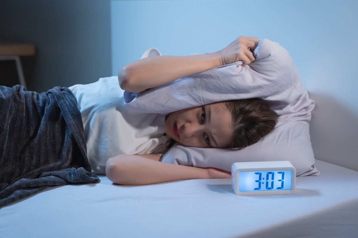 A man clutching his pillow to his head in exasperation as he struggles to sleep.