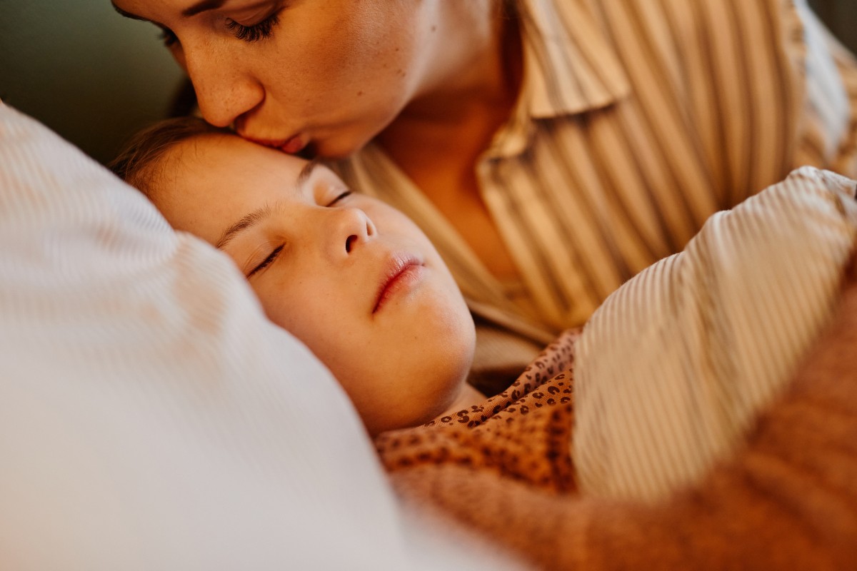 A mum kissing her child goodnight after they have fallen asleep