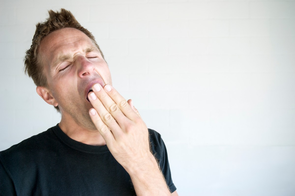 A man, standing alone stifling a yawn