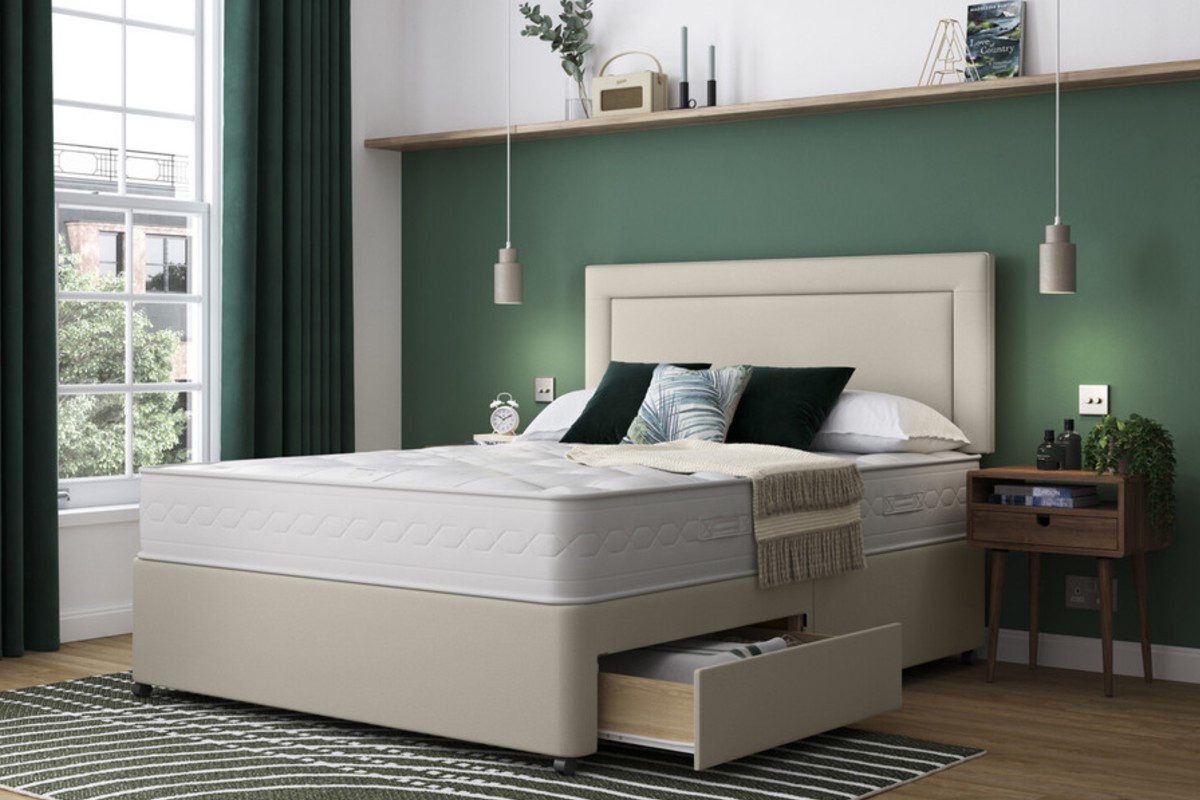 A neatly styled bedroom features a modern upholstered bed with an open storage drawer and warm green, beige and wooden accents.