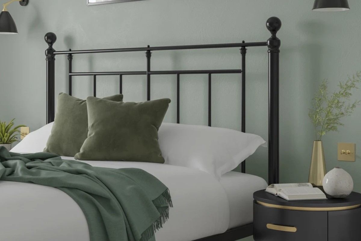 A neatly made bed frame with green accents sits in a calm, modern bedroom with matching black‑and‑gold decor.
