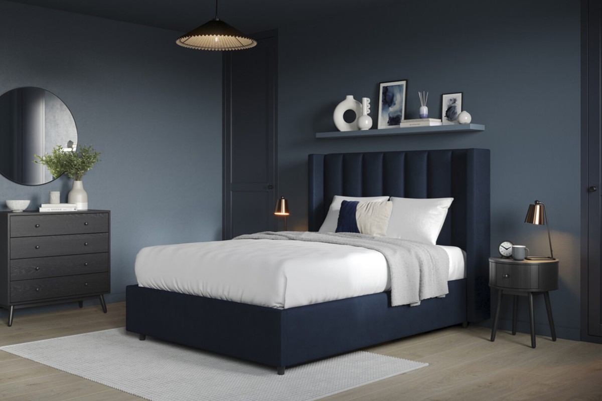 A navy blue bed frame set against mid blue walls paired with light wooden flooring