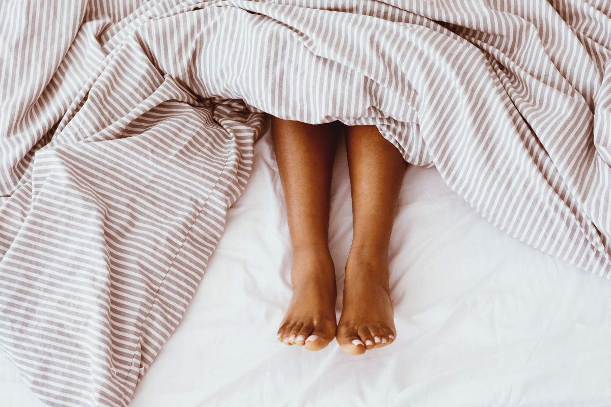A woman's legs poking out of the bottom the bed as her bedsheets have scrunched up during the night