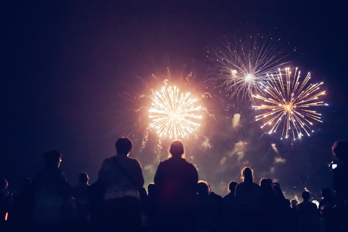 A family sat silhouetted against the night sky which is alight with fireworks.