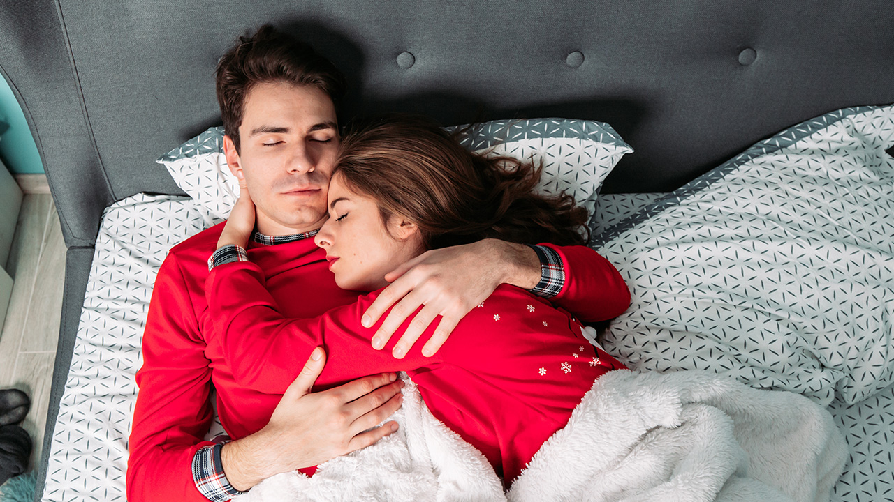 A couple snuggled together in bed wearing matching pyjamas