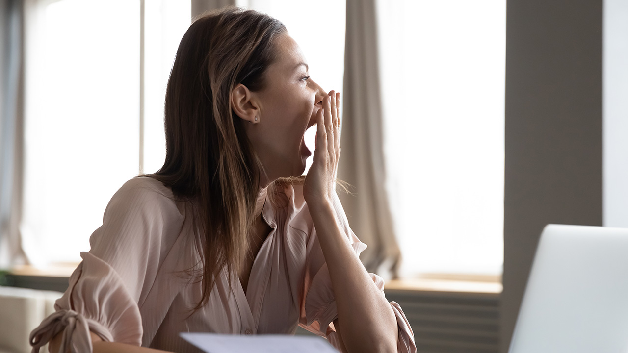 A woman yawning while covering her mouth while working on her computer