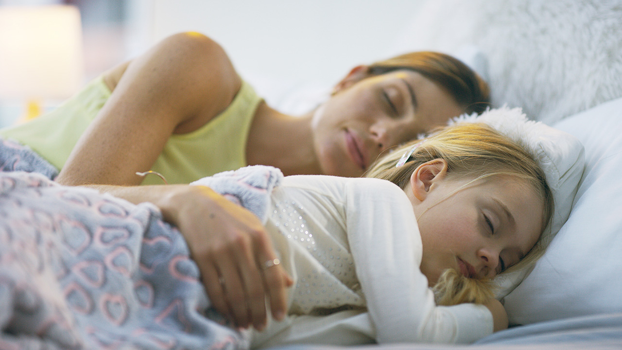 image of woman in bed with her daughter with her arm protectively over her as they both sleep on their sides