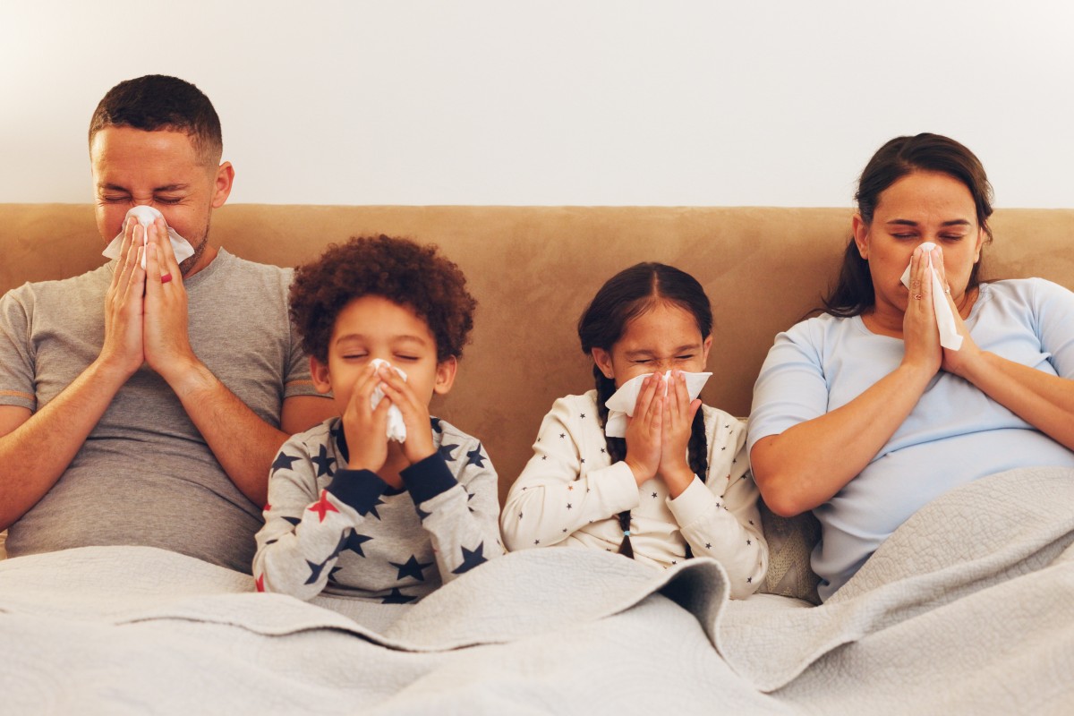 A family of four sat up in bed, all blowing their noses
