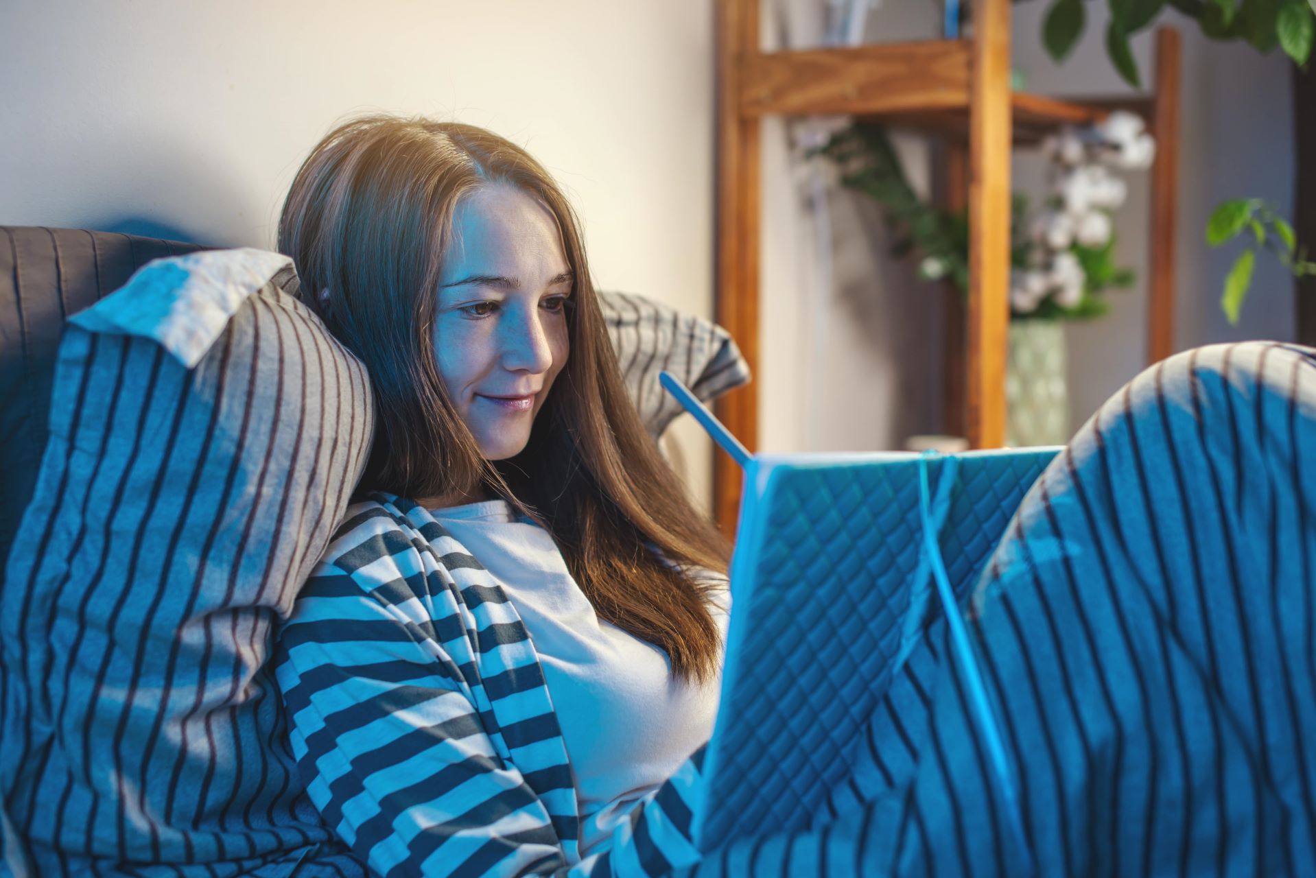 A lady sitting in bed. She is filling out her sleep diary before switching out the lights.