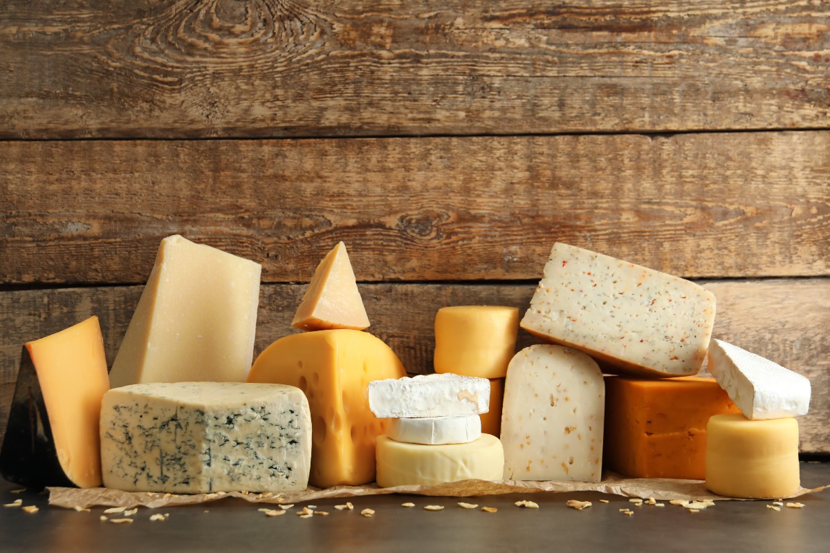 Various different types of cheeses laid out against a wooden boarded background
