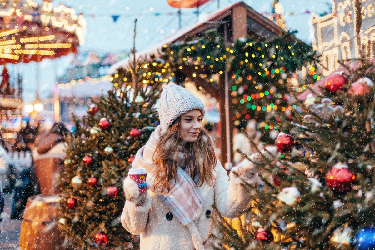 A lady wandering through the Christmas markets with the Christmas lights twinkling and snow falling all around her.