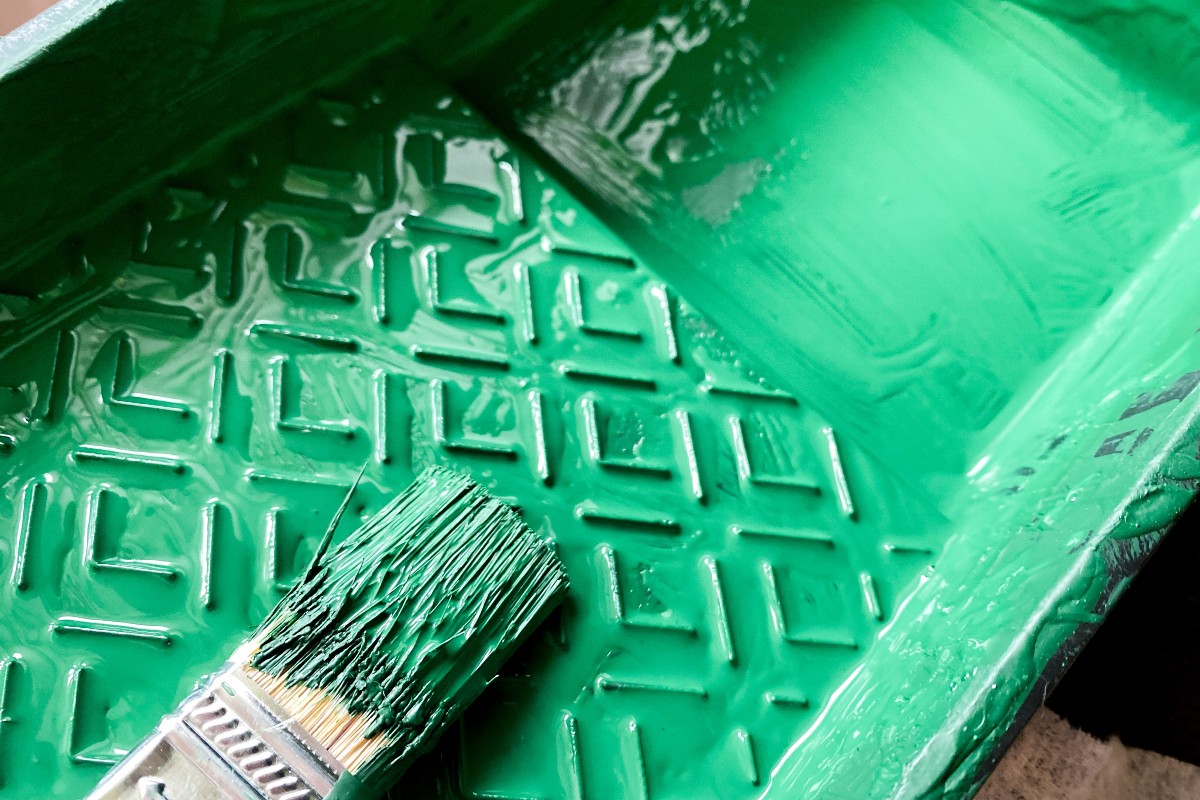 A paintbrush resting on a paint tray coated in a vibrant green.