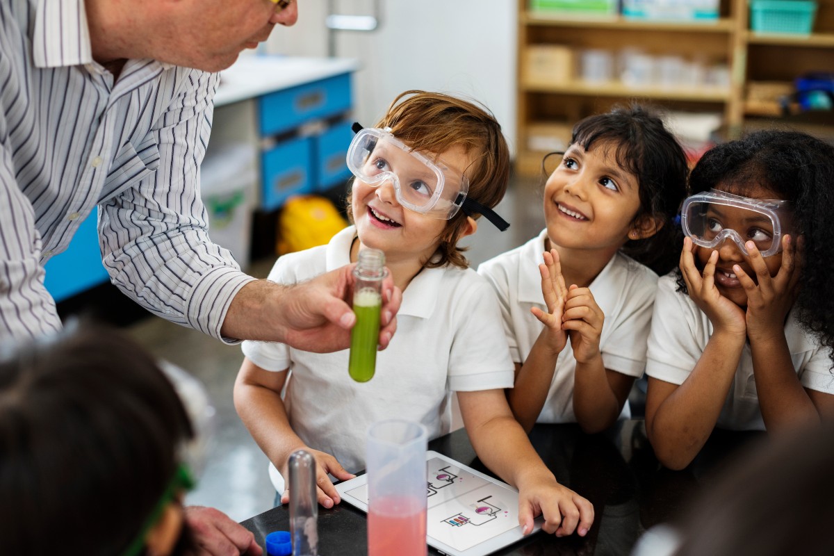 4 children gathering around a science teacher in exitement