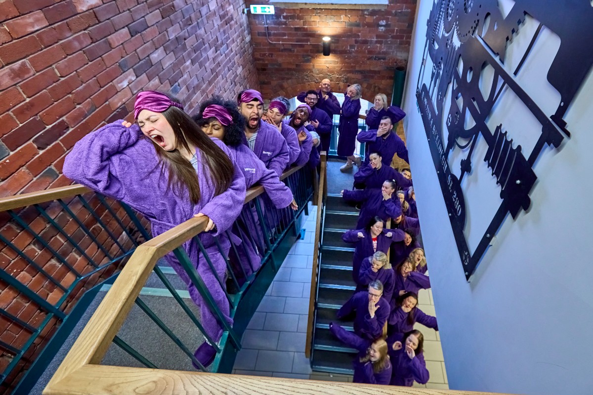 A long line of contagious yawners making their way up a winding staircase to the office while donning purple dressing gowns.