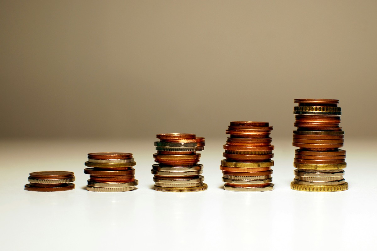 A tiered set of piles of coins including copper, silver and gold coins; starting small on the left and getting larger and larger as it moves towards the right