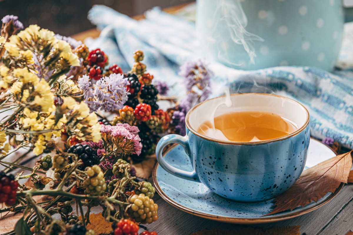 A cup of herbal tea sat on a saucer beside a bunch on dried flowers on a wooden tabletop.