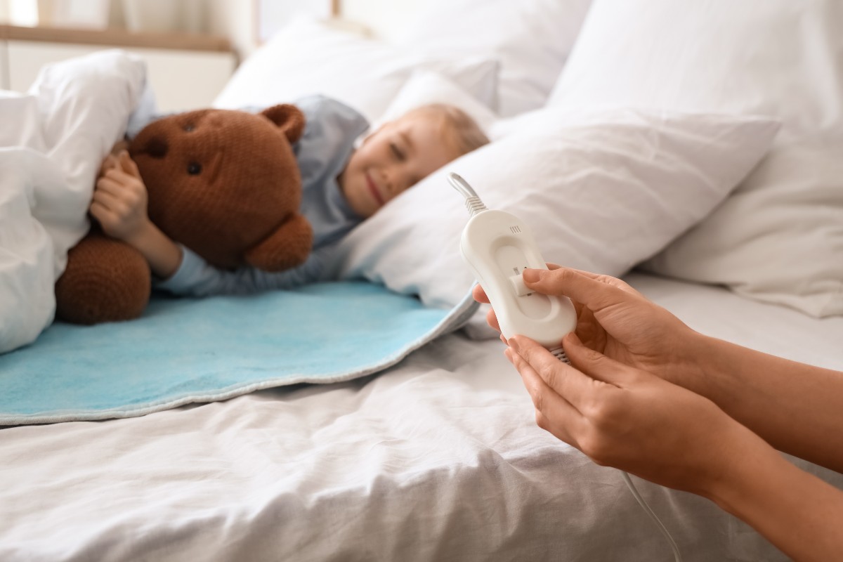 A child sleeping soundly atop an electric blanket while a parent adjusts the heat setting using the control.