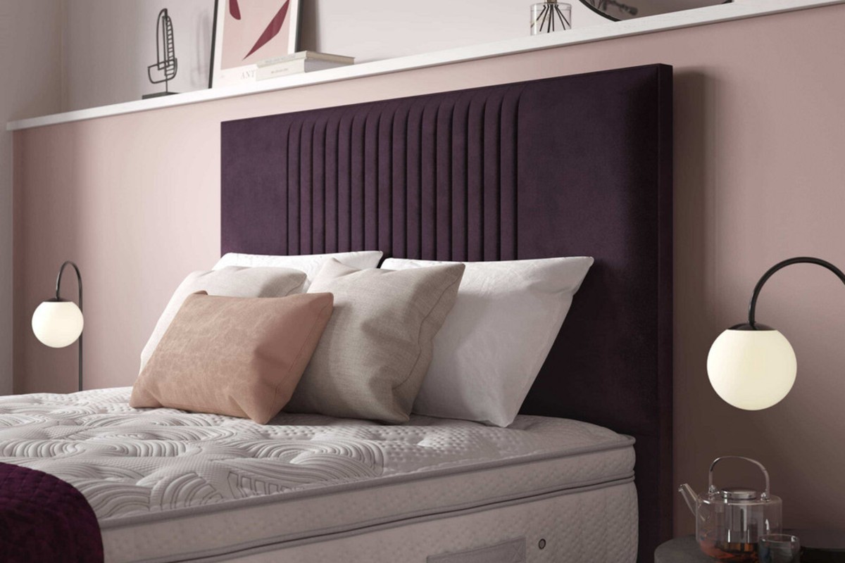 A close up of a purple headboard with pillows propped against it