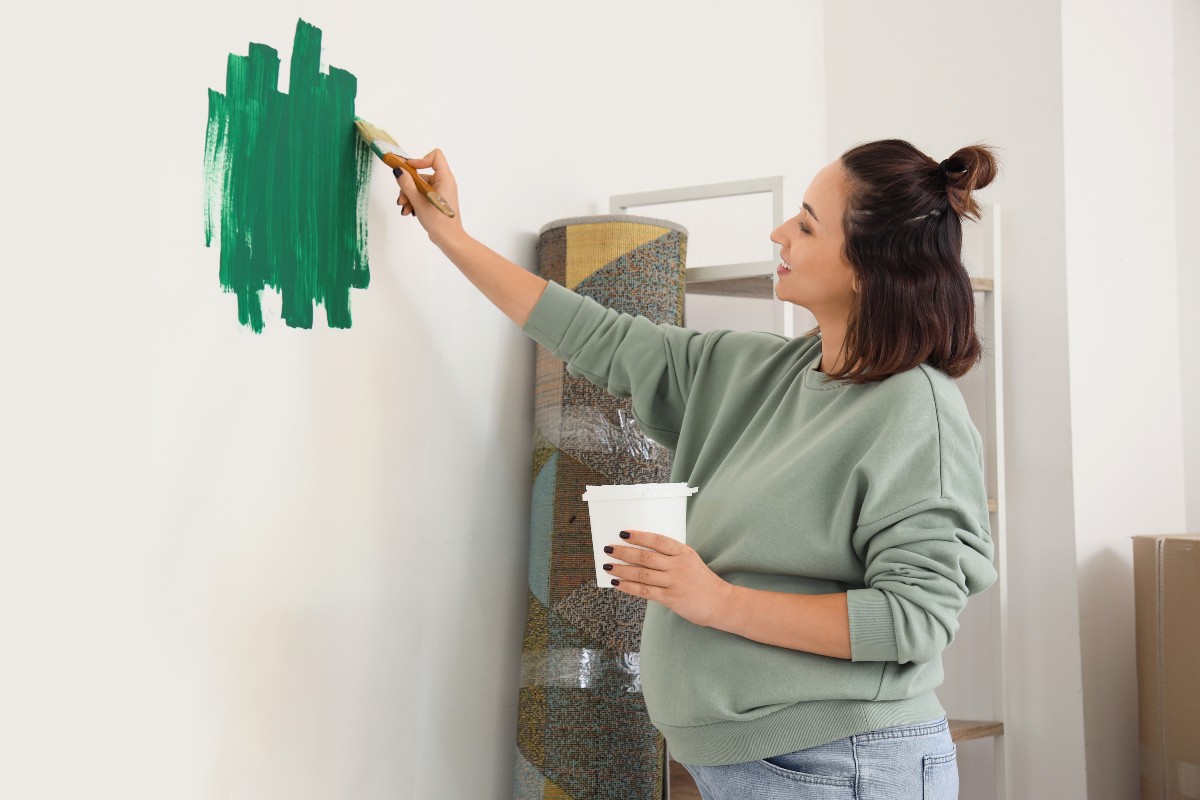 A mum-to-be painting the small nursery bedroom with bold green paint
