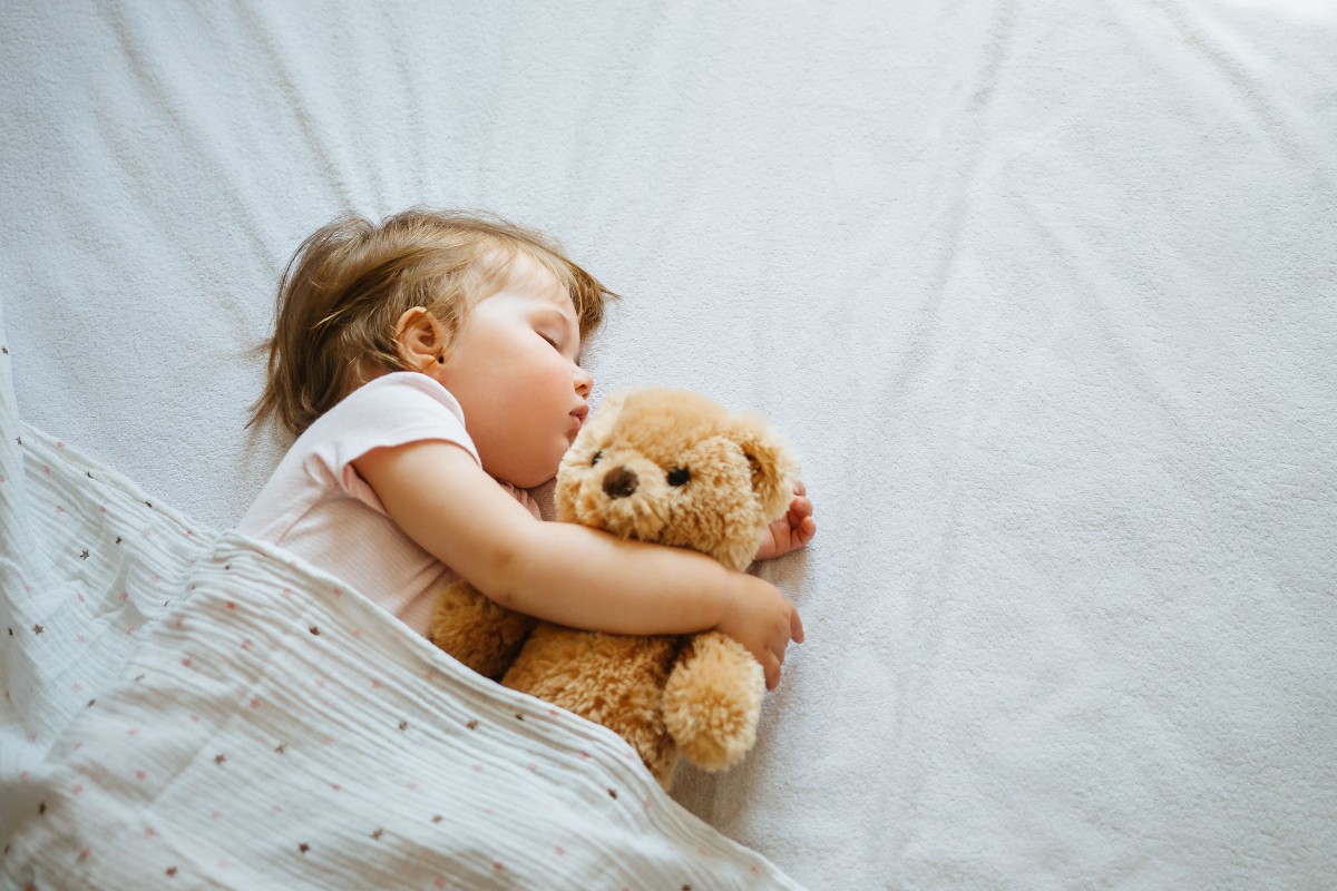 A sleeping baby lying on her side, cradling her teddy.