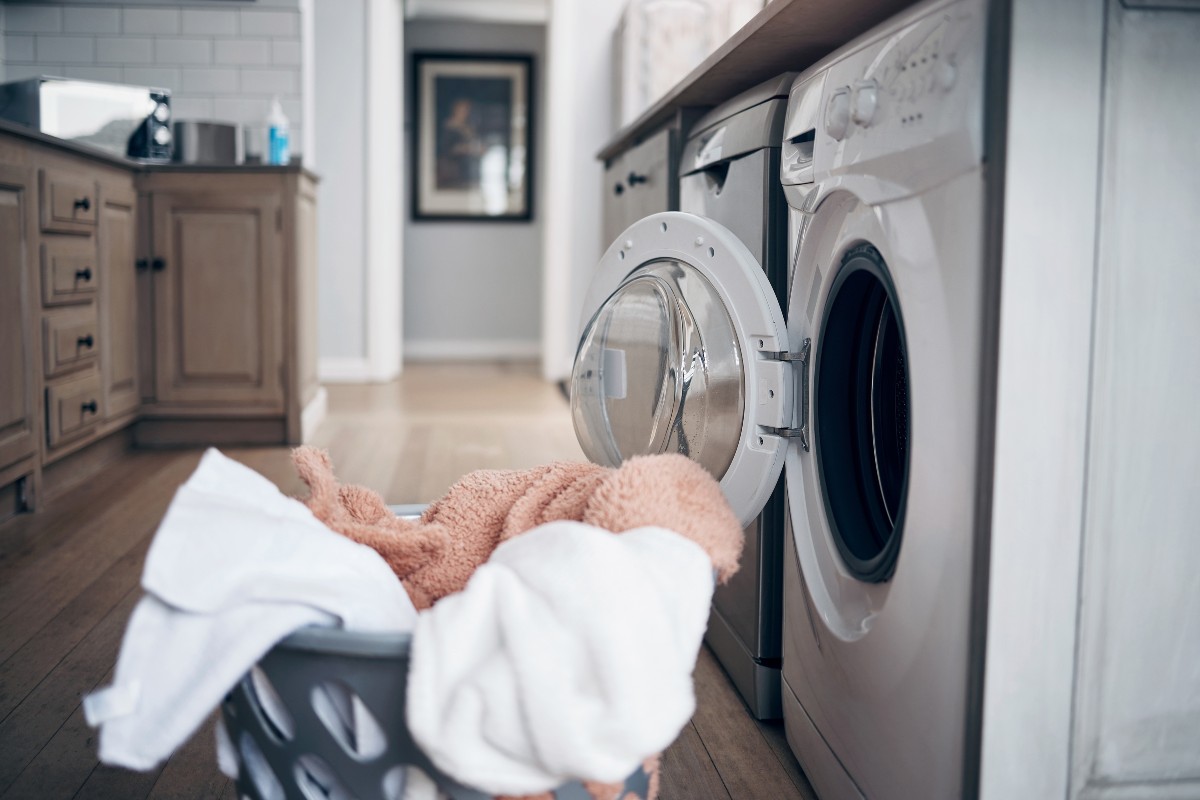 A washing basket full of bedding in front of the open door of a washing machine.