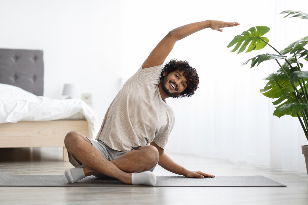 A man sat crossed legged on the floor stretching in a yoga pose while enjoying his morning mindfulness meditation