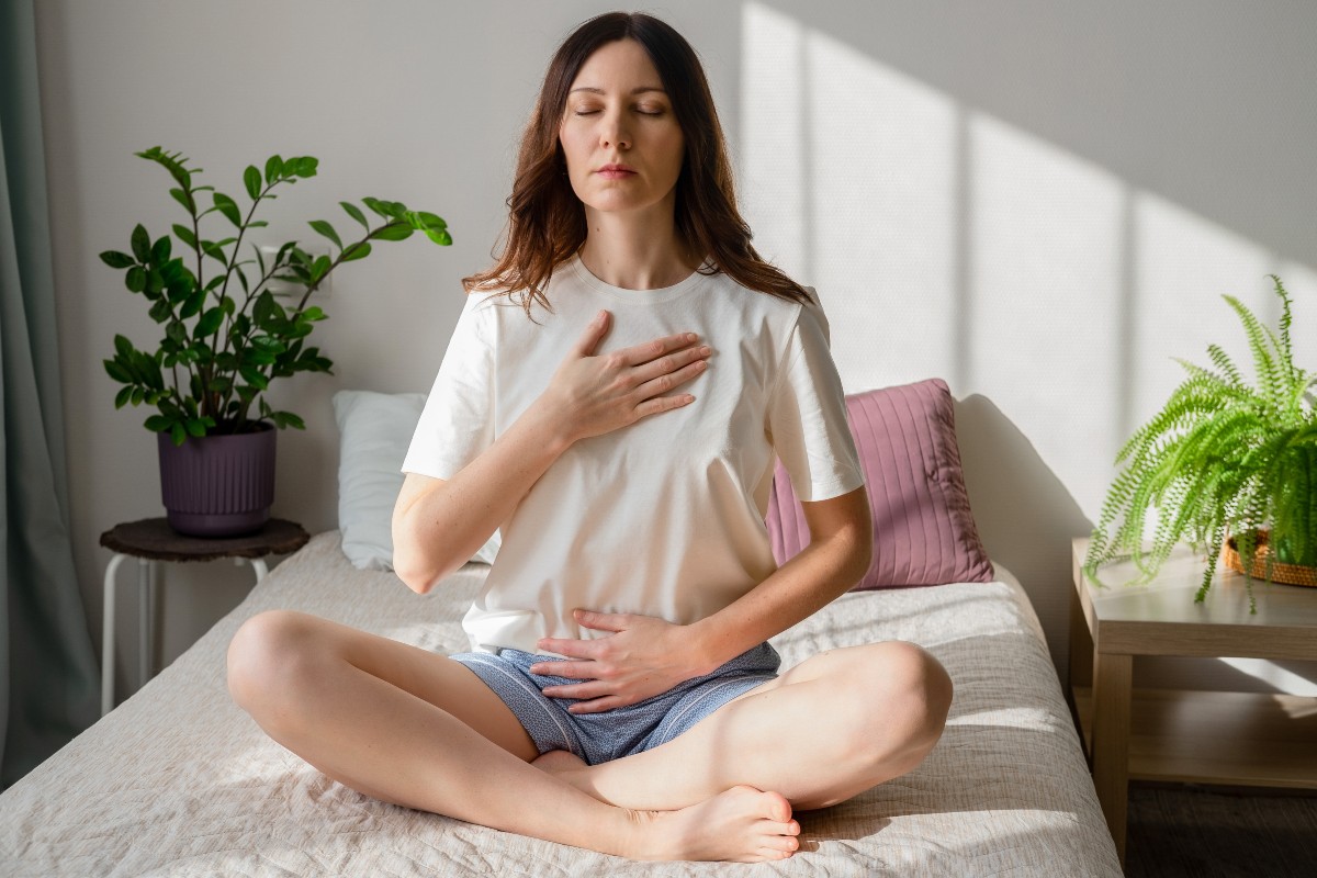 A woman sat with her legs crossed on her bed while practicing yoga breathing exercises.