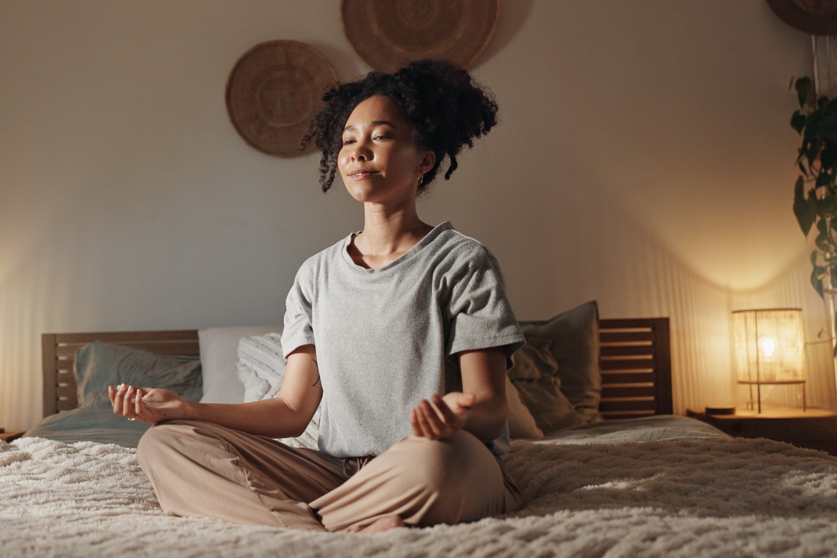 A lady sat cross legged in bed in the morning practicing mindful meditation