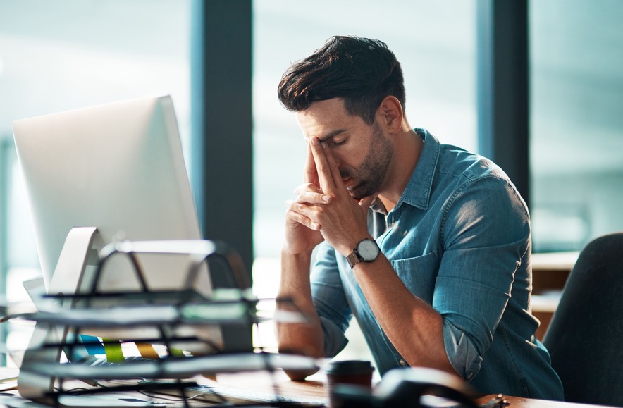 A man rubbing the bridge of his nose after a stressful work morning at his laptop.