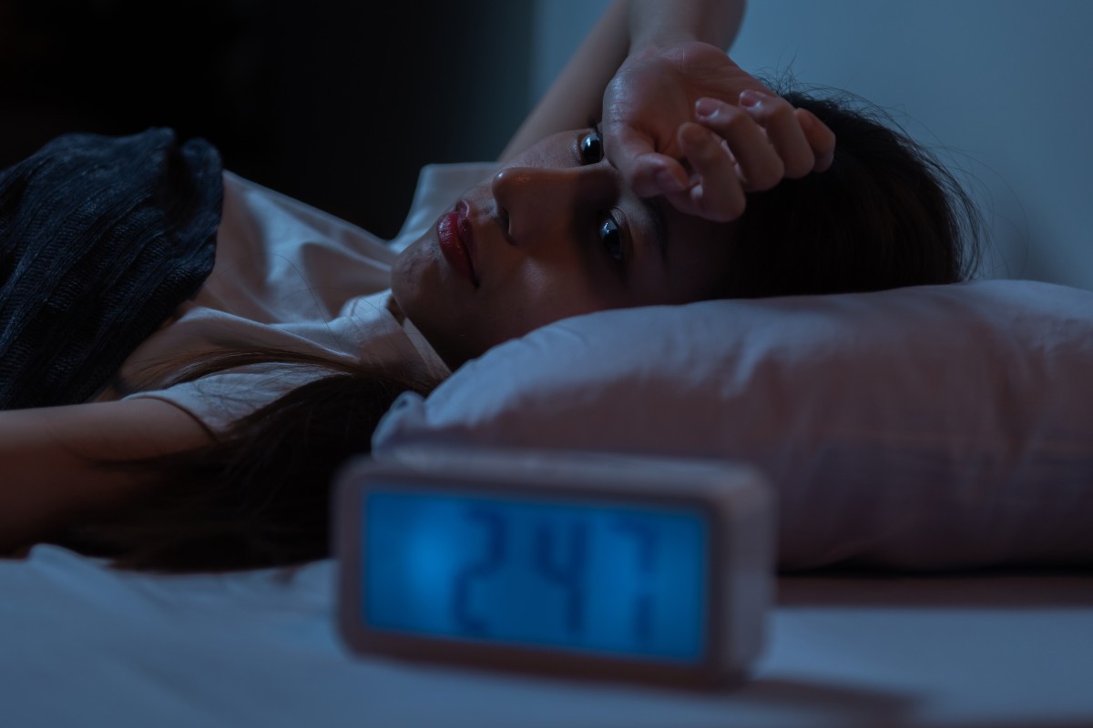 A person lying awake in bed, the time on the digital alarm clock reads 2:47am