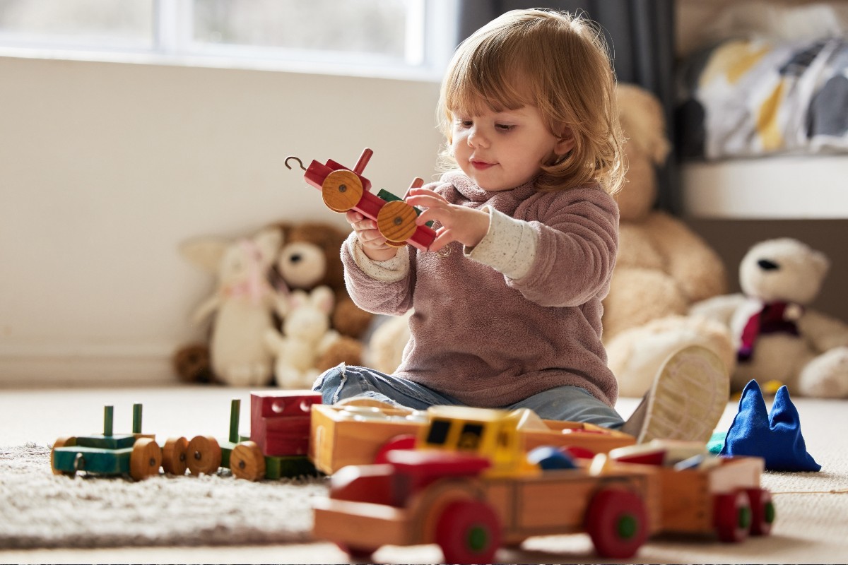 A child sat on the floor playing with a wooden train and some wooden building blocks