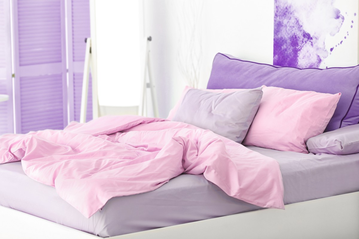 A bed set in a white bedroom featuring accents of pale pink and pale purples