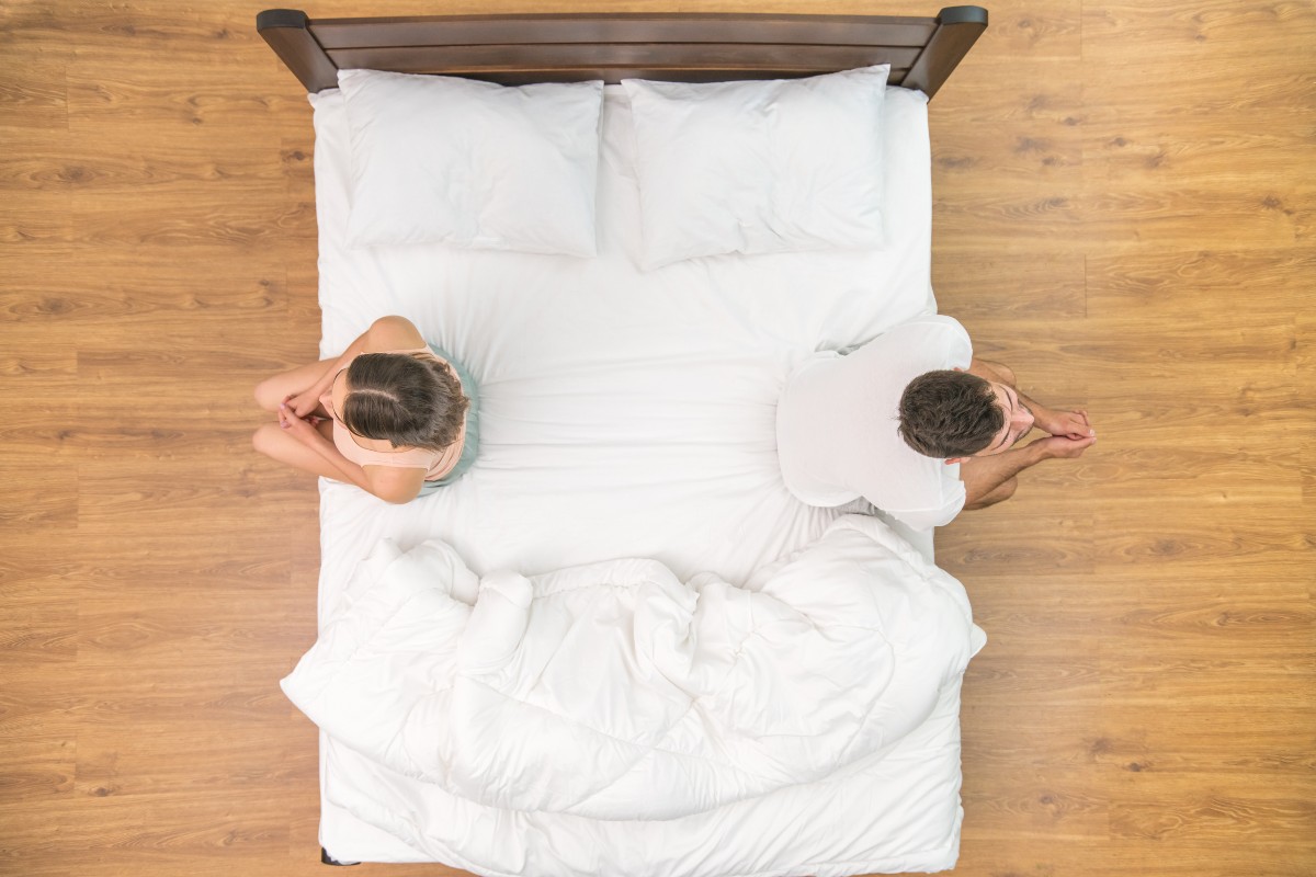 A couple sat on their bed, backs to one another, feet on the floor after another bedtime battle