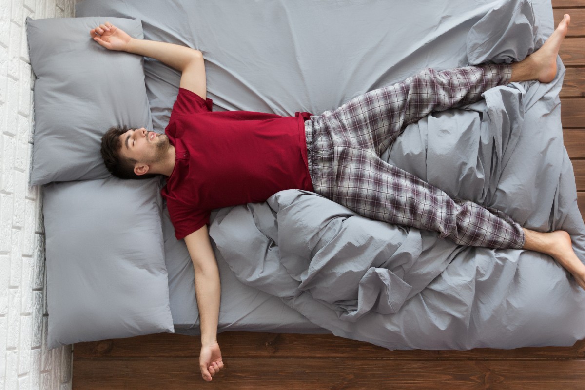 A man asleep on his back, star-fishing with legs and arms spread wide.