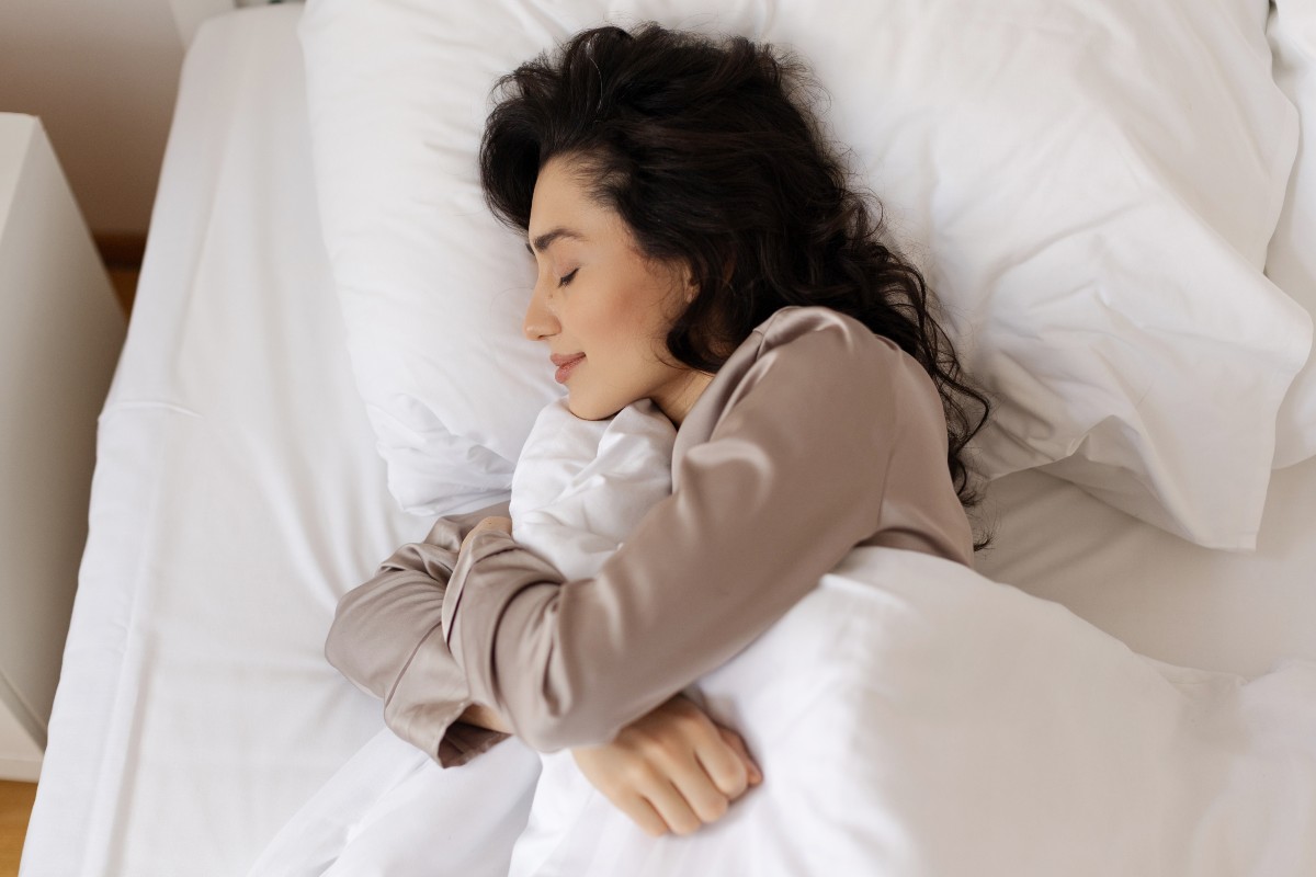 A woman asleep on her side in bed, hugging a pillow