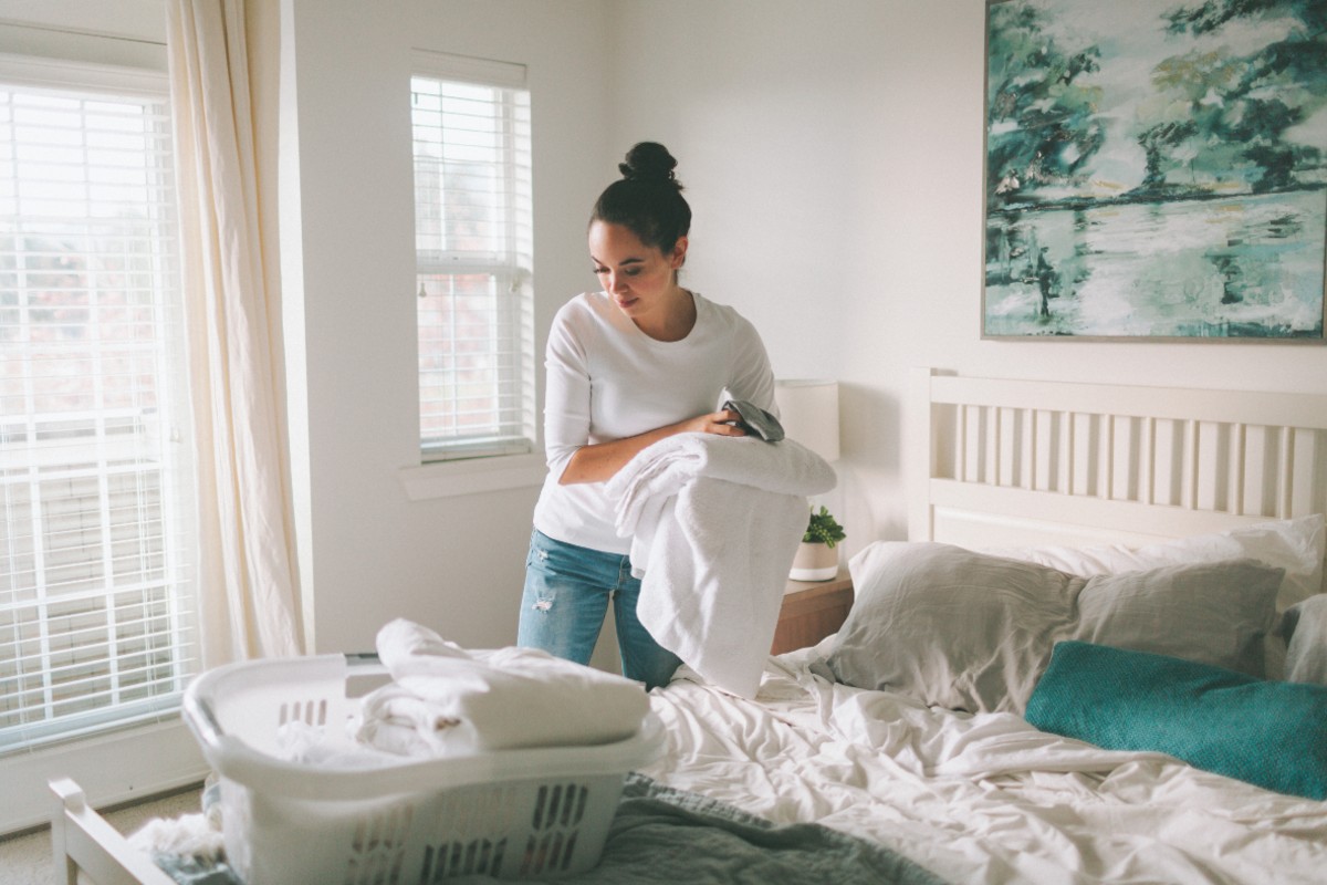 A lady folding laundry on her bed as the spring daylight filters through her window.