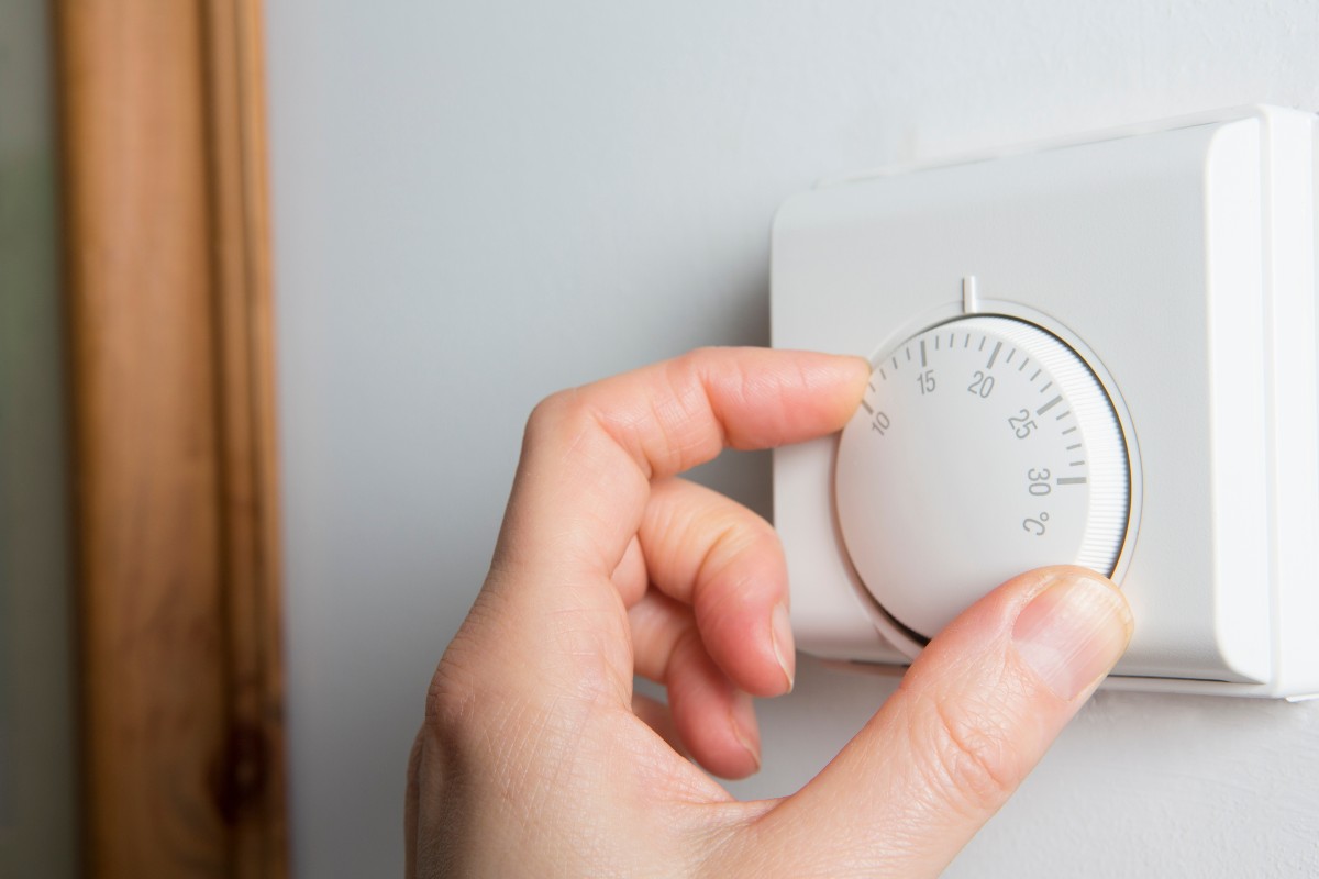 A person turning the temperature down on their thermostat.
